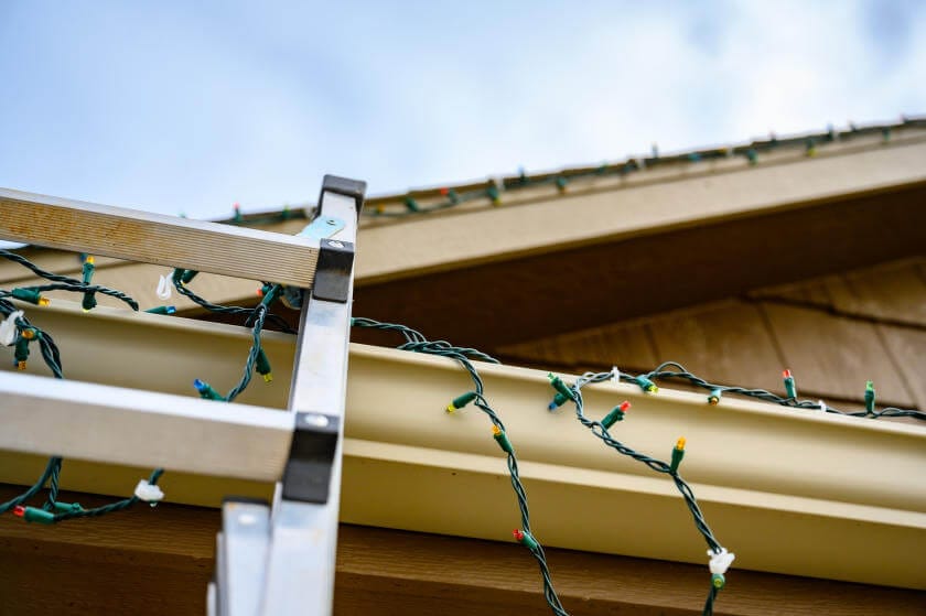 A string of Christmas lights being attached to house gutter