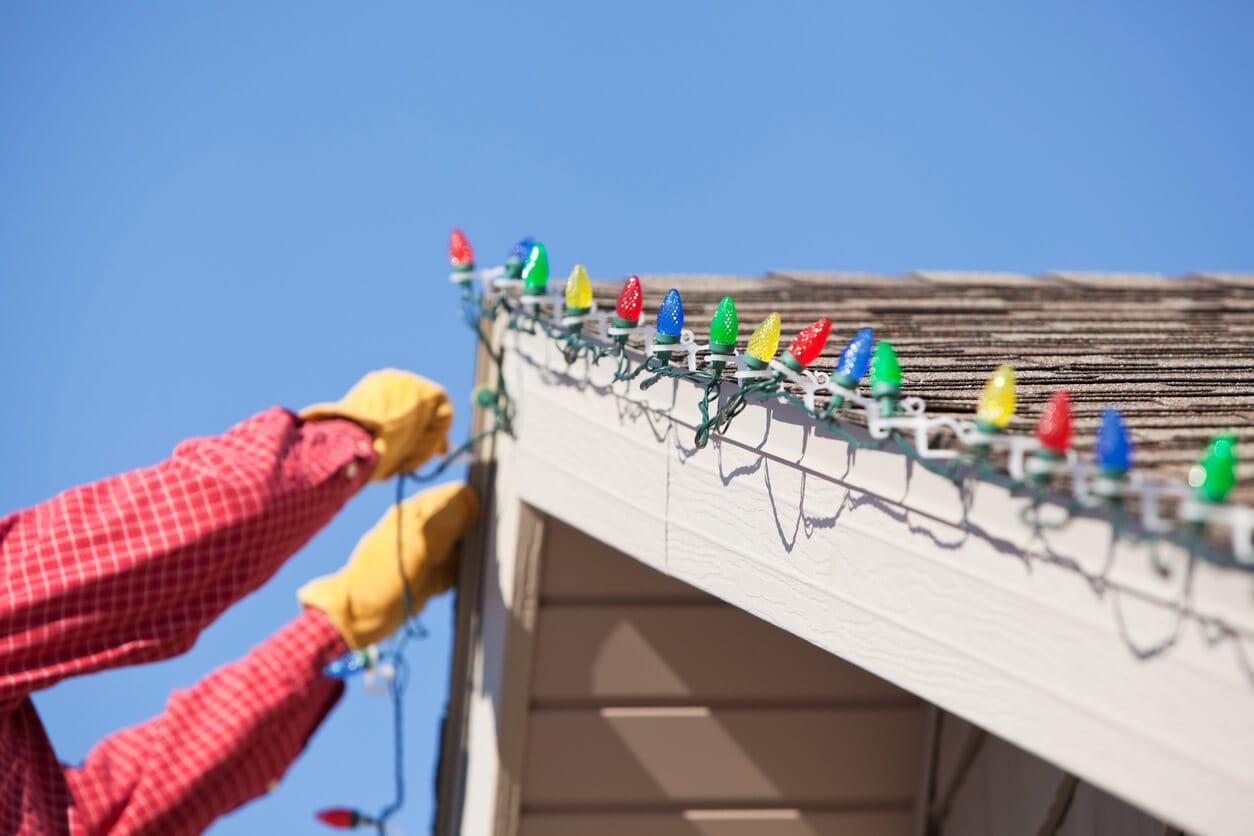Person attaching Christmas lights to the house roof