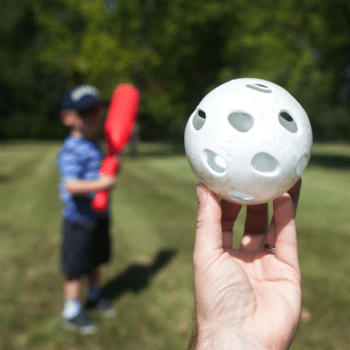 A hand holding a white wiffle ball