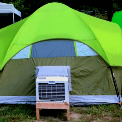 Portable tent air conditioner attached to a green tent