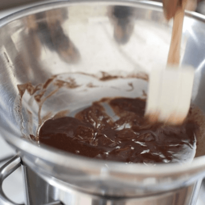  Person stirring melted chocolate in a stainless steel bowl