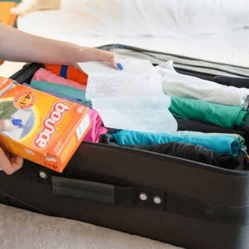 Person using scented dryer sheets to rid suitcase of odors