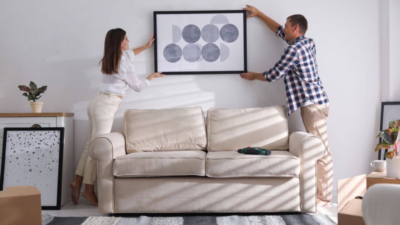 Two people hanging wall art behind a sofa
