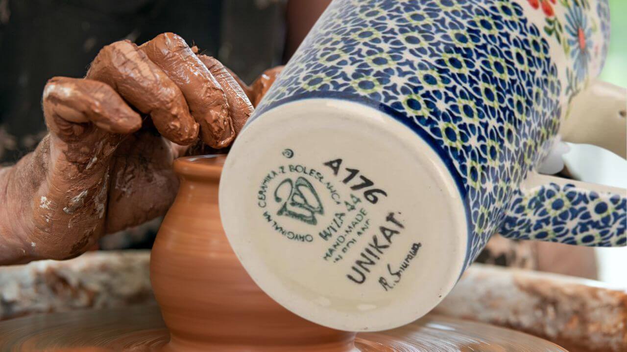 Looking at the bottom of a handmade ceramic mug in front of a person working a pottery wheel