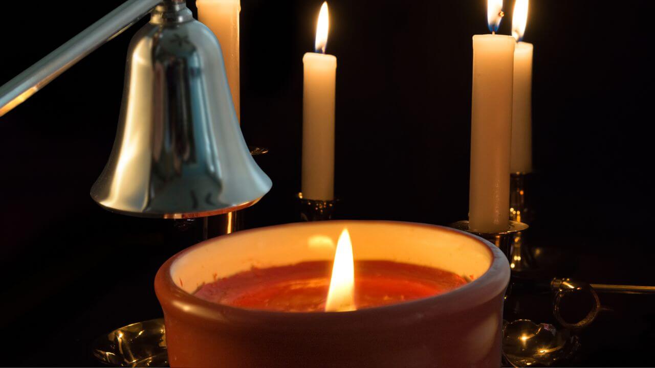 Candle snuffer over a lit candle in front of a candelabra with lit candles