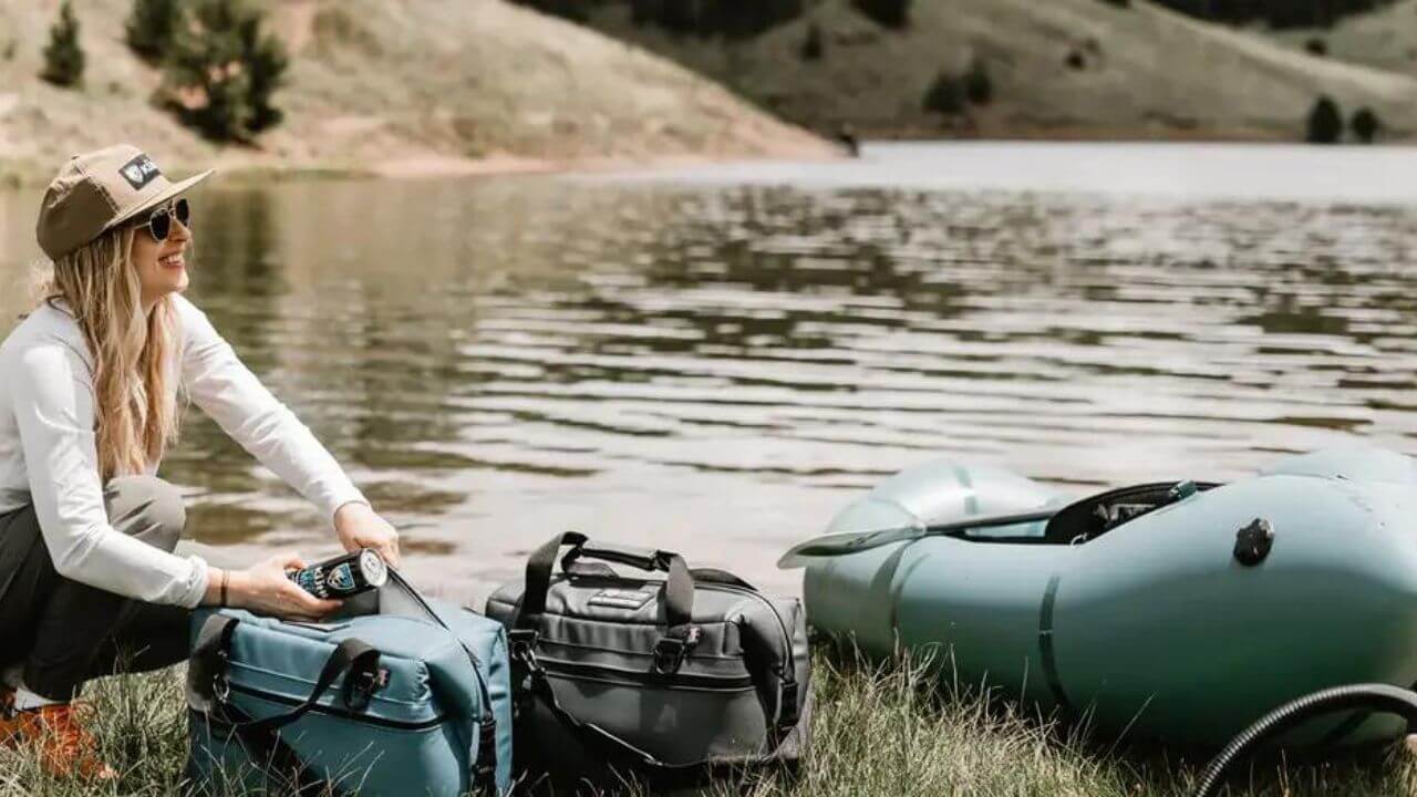 Woman with kayak coolers next to her kayak on a riverbank