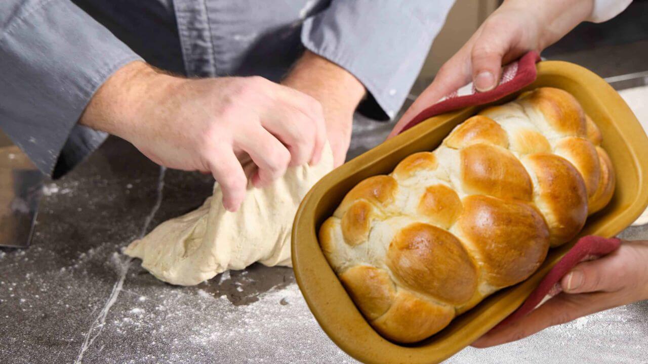 Ceramic baking dish with baked bread in front of someone kneading bread dough