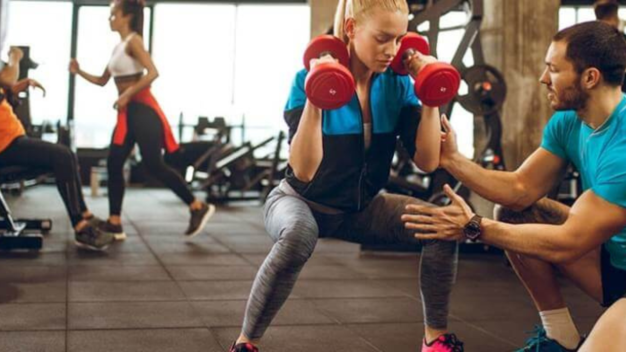 Woman exercising with dumbbells to build muscle while trainer observes